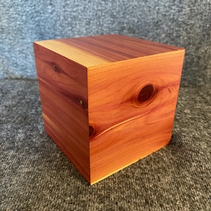 May include: A solid wood cube box made of cedar wood. The box has a natural reddish-brown color and a smooth finish.
