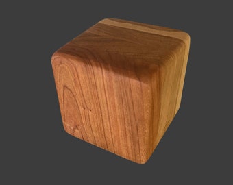 May include: A small, wooden cube with a light brown color and a darker brown stripe across the top.