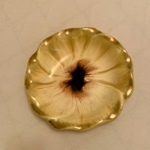 Könnte beinhalten: Eine dekorative, blütenförmige Schale mit gewelltem Rand. Die Schale hat eine cremefarbene gelbe Außenseite mit einem dunkelbraunen Zentrum, das einer stilisierten Blume ähnelt. Die Schale ist wahrscheinlich aus Keramik oder Porzellan.