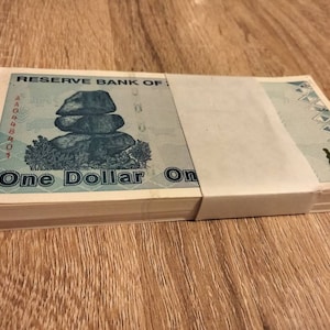 Pode incluir: Uma pilha de notas novas, nítidas, azuis e brancas de um dólar do Banco da Reserva de Fiji. As notas apresentam uma pilha de pedras e o texto "One Dollar One".