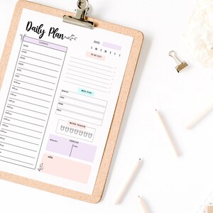 May include: A daily planner with a corkboard backing. The planner has sections for a schedule, a to-do list, a meal plan, a water tracker, and a mood tracker. The planner is on a white surface with pencils and a binder clip.