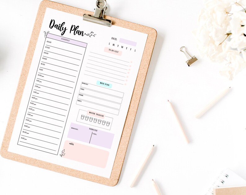 May include: A daily planner with a corkboard backing. The planner has sections for a schedule, a to-do list, a meal plan, a water tracker, and a mood tracker. The planner is on a white surface with pencils and a binder clip.