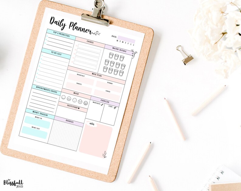 May include: A printable daily planner with sections for top priorities, to do list, appointments, money tracker, meals, mood, gratitude, exercise, and water intake. The planner is on a corkboard with a clip.