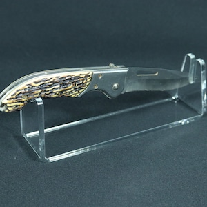 May include: A clear acrylic knife display stand with a single folding knife with a brown and tan stag horn handle.