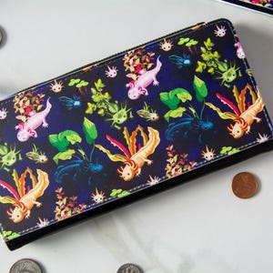 May include: A black wallet with a colorful axolotl pattern. The design features pink, orange, and yellow axolotls, along with green plants and other aquatic elements. The wallet has a silver zipper and a matching axolotl charm.