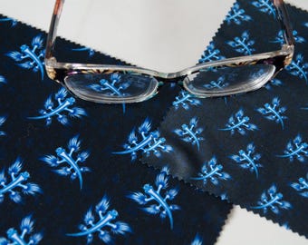 May include: Eyeglasses with a patterned frame rest on two dark blue microfiber cloths. The cloths are decorated with a repeating pattern of stylized blue sea creatures. The glasses have clear lenses.