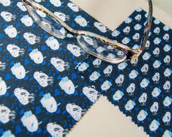 May include: Eyeglasses with a patterned frame rest on a navy blue fabric with a repeating white and blue floral design. The fabric has a scalloped edge. The glasses have clear lenses.