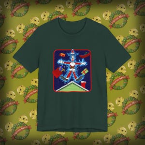 May include: A dark green short-sleeve t-shirt featuring a graphic print of a cartoon character dressed as Santa Claus, positioned in a star shape above a house roof. The character is surrounded by floating gift boxes and a red sack on a blue background.