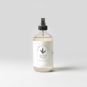 May include: A clear glass spray bottle with a black nozzle and a white label. The label features the text "DSAR CANDLE CO" and "Spiced Bamboo Room Spray". The bottle contains a light-coloured liquid and is approximately 237 ml.