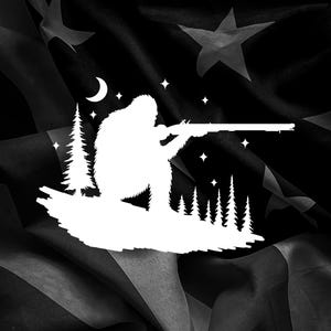 May include: A black and white graphic featuring a silhouette of Bigfoot aiming a rifle. The design includes a crescent moon, stars, and pine trees, set against a backdrop resembling the American flag.