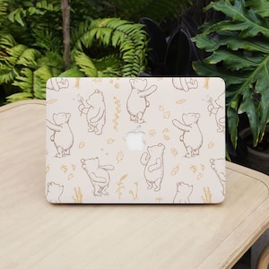 以下が含まれることがあります： クリーム色のラップトップケースで、タンポポを吹くクマの茶色の線画が繰り返し描かれたパターンになっています。ケースにはアップルのロゴが見えます。