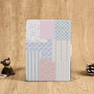 May include: A tablet case with a patchwork design, incorporating floral, striped, and checkered patterns in pastel shades of pink, blue, and white. The case is closed and has a magnetic clasp. The background is a wooden surface.
