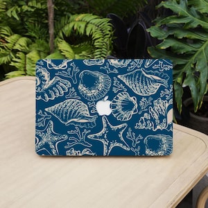 May include: A dark blue laptop skin featuring a repeating pattern of cream-colored seashells, starfish, and coral branches. The design includes a central cutout revealing the silver Apple logo on the laptop lid, creating a nautical aesthetic.