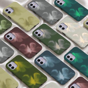 Könnte beinhalten: Eine Sammlung rechteckiger Smartphone-Hüllen mit einem weich gezeichneten, ätherischen Blumenmuster. Jede Hülle verfügt über einen Ausschnitt für eine Doppelkamera und ist in verschiedenen gedeckten Farben wie Salbeigrün, Anthrazit, Dunkelblaugrün und Altrosa erhältlich.