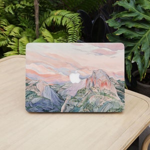 May include: A laptop case featuring a watercolor painting of a mountain landscape with a sunset sky. The case has a white Apple logo and a design with shades of pink, blue, green, and gray.