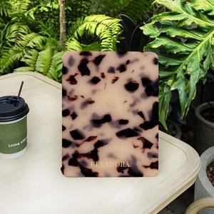 May include: A rectangular electronic reader case featuring a beige and dark brown tortoiseshell pattern with the name ELEANORA printed in gold lettering near the bottom centre. The case has rounded corners and a smooth, matte-like finish.