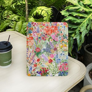 May include: A rectangular tablet case featuring a vibrant floral pattern with a variety of colorful flowers. The design includes red, pink, blue, and purple blooms. A coffee cup with the text "Living with" is on the left.