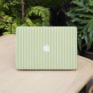May include: A laptop featuring a green and white striped pattern. The laptop displays the Apple logo in white. It rests on a light brown wooden surface, with green plants in the background.