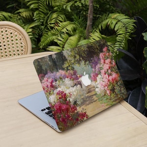 May include: A laptop with a floral design case featuring a garden scene with pink, white, and purple flowers. The laptop is open on a wooden table, with green foliage in the background.