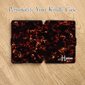 May include: A Kindle case featuring a black and fiery orange marbled pattern. The text "Personalize Your Kindle Case" appears at the top, and the name "ADA Hanna" is printed in white script on the bottom right corner of the cover.