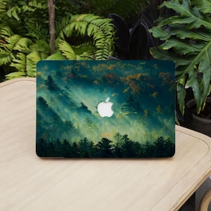 May include: A laptop cover with a forest scene and a white Apple logo. The design depicts a misty forest with green and orange trees, and sun rays filtering through the trees.