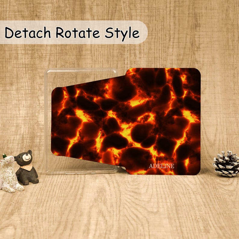 May include: A rectangular phone grip with a fiery lava pattern featuring glowing orange and yellow veins against dark brown and black shapes. The text "Detach Rotate Style" appears at the top, and the name "ADELINE" is printed in white at the bottom.