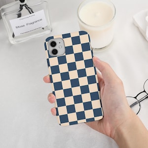 May include: A phone case with a blue and beige checkerboard pattern. The case is held in a hand, with a clear perfume bottle and a lit candle in the background. The phone case has a camera cutout.