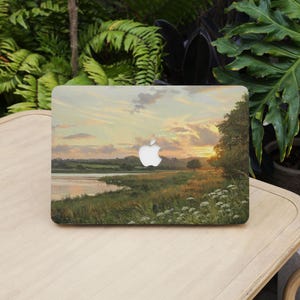 Peut inclure: Housse d'ordinateur portable avec une peinture de paysage d'un coucher de soleil sur une rivière et un champ herbeux. Le design comprend un logo Apple blanc. L'œuvre représente une scène naturelle sereine avec des couleurs chaudes.