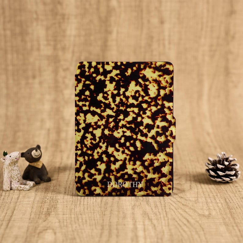 May include: A rectangular e-reader case featuring a brown and yellow tortoiseshell pattern. The name DOROTHY is printed in small white capital letters near the bottom center of the front cover. The case has a smooth, glossy finish.