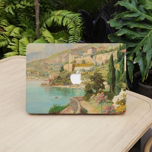 Puede incluir: Funda para portátil con una pintura vintage de un pueblo costero, edificios en una ladera, un mar en calma y un pequeño barco. La obra de arte tiene una paleta de colores suaves con tonos verdes, azules y beige. El logotipo de Apple es visible.