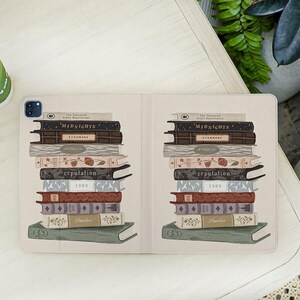 May include: An open tablet case featuring a stack of illustrated books. The books are in various colors, including brown, red, and beige, with titles like "MIDNIGHTS," "EVERMORE," "reputation," and "Fearless." The case is beige with a white background.