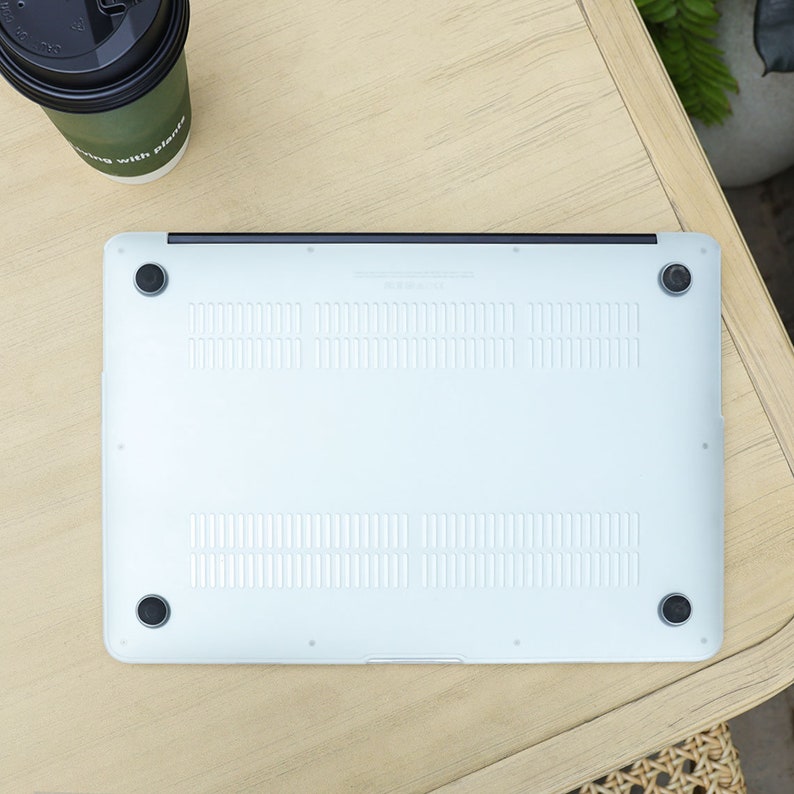 May include: A silver laptop computer with a black hinge and four black rubber feet. The bottom of the laptop has ventilation slots and small circular rubber feet. A coffee cup with the text "living with plants" is in the upper left corner.