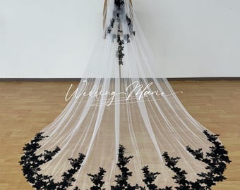 May include: A long, white bridal veil with intricate black floral lace detailing along the edges and cascading down the back. The veil is displayed on a mannequin, showcasing its length and design. The text "Wedding Marie" is visible.