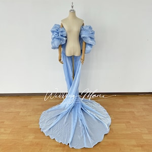 Puede incluir: Un vestido de maternidad azul claro con mangas abullonadas grandes y una cola fluida. El vestido se exhibe en un maniquí. El texto "Wedding Marie" está escrito en cursiva en la parte inferior de la imagen.