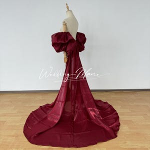 Puede incluir: Un vestido de noche burdeos con un gran lazo en la espalda y una larga cola. El vestido se exhibe en un maniqu&iacute;, destacando su elegante dise&ntilde;o y su lujoso tejido. El texto "Wedding Marie" es visible.