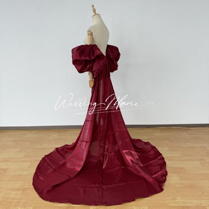 Puede incluir: Un vestido de noche burdeos con un gran lazo en la espalda y una larga cola. El vestido se exhibe en un maniqu&iacute;, destacando su elegante dise&ntilde;o y su lujoso tejido. El texto "Wedding Marie" es visible.
