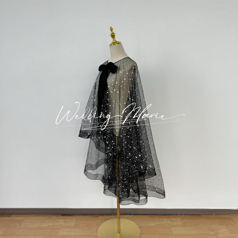 May include: A black tulle cape with silver glitter stars. The cape has a black satin bow at the neck.