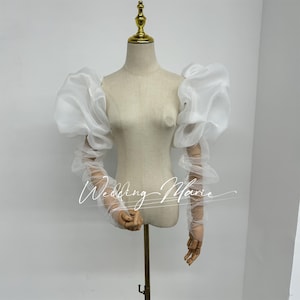 May include: White tulle bridal sleeves with puffed shoulders. The sleeves are gathered at the elbow and wrist, creating a romantic and elegant look.