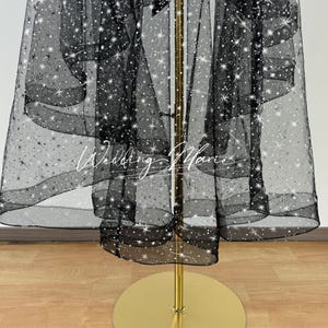 May include: Black tulle fabric with white glitter stars. The fabric is draped over a gold stand.