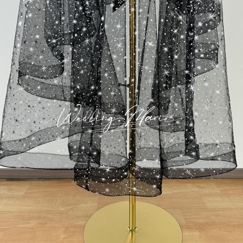 May include: Black tulle fabric with white glitter stars. The fabric is draped over a gold stand.