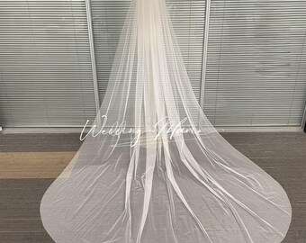 May include: A long, flowing white bridal veil. The veil is made of a sheer, lightweight fabric and drapes to the floor. The veil is displayed on a mannequin. The text "Wedding Mania" is visible on the veil.