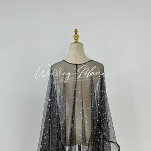 May include: A black sheer cape with a sparkly design. The cape is made of a fine mesh fabric and has a loose, flowing fit.