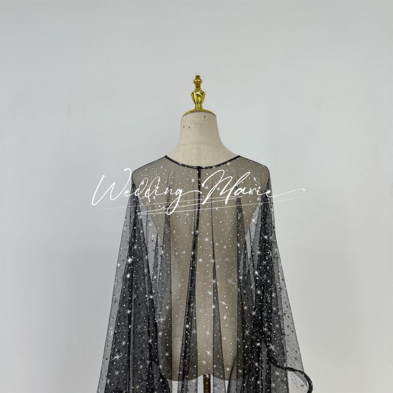 May include: A black sheer cape with a sparkly design. The cape is made of a fine mesh fabric and has a loose, flowing fit.