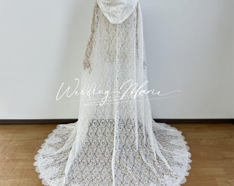May include: A white lace hooded cape with a long train, displayed on a mannequin. The cape features an intricate floral lace pattern and a scalloped edge on the train. The text "Wedding Marie" is written on the cape.