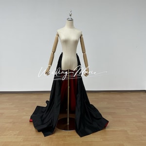 May include: A black and red skirt with a long train. The skirt is being displayed on a mannequin.