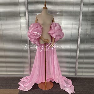 May include: A light pink gown with voluminous, off-the-shoulder sleeves and a flowing skirt. The dress is displayed on a mannequin, with the text "Wedding Marie" in a script font across the front. The fabric has a slight sheen.