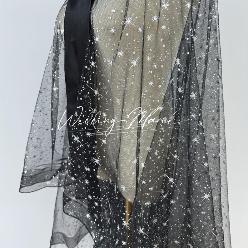 May include: Black tulle fabric with a white star pattern. The fabric is sheer and has a delicate texture.