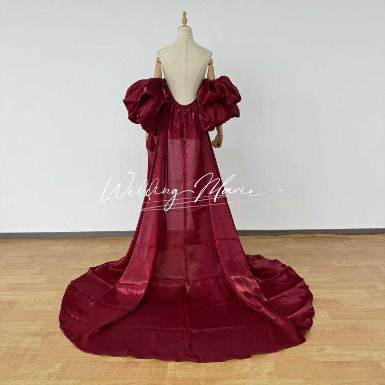 Puede incluir: Un vestido de noche burdeos con una larga cola y espalda descubierta se exhibe en un maniqu&iacute;. El vestido presenta mangas abullonadas grandes. El texto "Wedding Marie" est&aacute; escrito en cursiva.