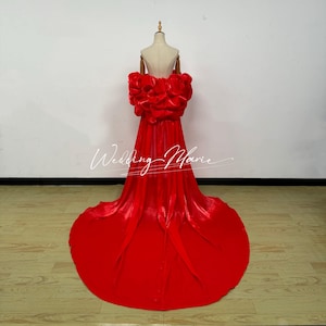 May include: A vibrant red formal gown with a dramatic train. The bodice features a large, ruffled floral design. The dress is displayed on a mannequin against a white background. The text "Wedding Marie" is written on the dress.