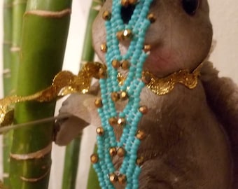 May include: A grey squirrel figurine wearing a turquoise beaded necklace. The necklace is made of small turquoise beads and gold accents. The squirrel is perched on a bamboo stalk.